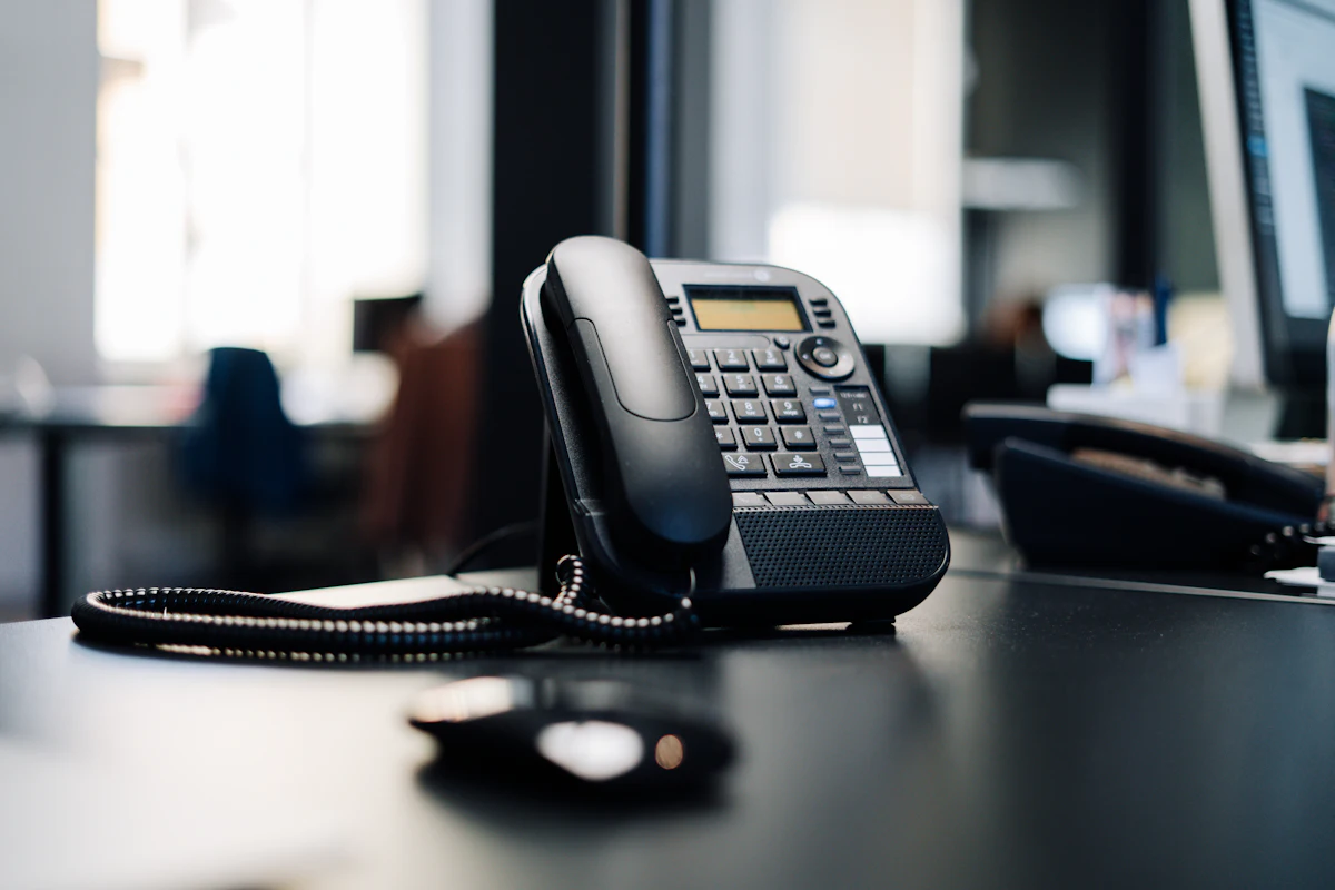 A black office desk phone, used for insurer calls and negotiations